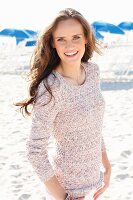 A young, long-haired woman on a beach wearing a knitted jumper