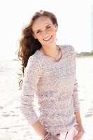 A young, long-haired woman on a beach wearing a knitted jumper