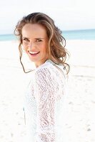 A young woman with long hair on a beach wearing a white lace dress