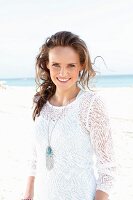 A young, long-haired woman on a beach wearing a white lace dress