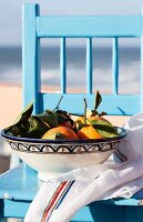 Orangen in einer Keramikschale auf hellblauem Stuhl am Meer