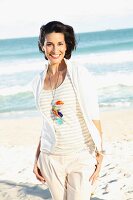 Dunkelhaarige Frau mit hellem T-Shirt und Jacke am Strand