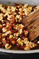 Roughly chopped walnuts being roasted with bacon