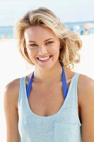 A young blonde woman on a beach wearing a blue tank top