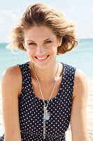 A young blonde woman on a beach wearing a sleeveless, polka-dot summer dress