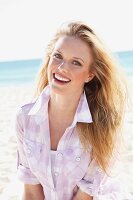 A young blonde woman on the beach wearing a purple and white checked blouse