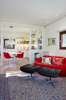 Glasschiebetür zwischen Essbereich und Wohnraum, rote Designercouch mit schwarzen Lederhockern