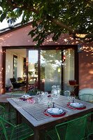 Set garden table below deciduous tree in front of open glass door in gable-end façade