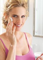 A blonde woman applying face cream