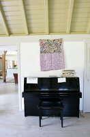 Black piano and bench in front of ethnic-style cloth bag hung on wall