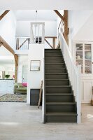 Dark wooden staircase with white balustrade in open-plan interior; view into kitchen to one side