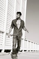 The young man wearing blue jeans and a denim shirt against a white wooden wall (black and white shot)