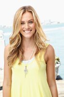 A blonde woman wearing a light yellow top and a fashionable necklace