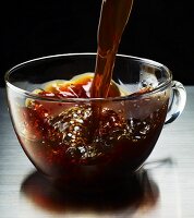Black coffee being poured into a glass mug