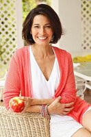 Dark-haired woman wearing top and cardigan holding apple