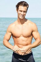 A muscular young man by the sea wearing blue bathing shorts