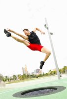 Mann beim Trampolin springen im Grünen vor Skyline