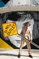 A young man wearing a light suit holding a 'NO OUTLET' street sign