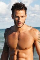 A young, topless, tattooed man by the sea
