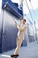 A young man wearing a light suit pulling on the chain of a rolling metal door