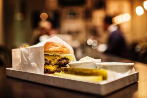 A hamburger, dips and gherkins on a tray on a counter