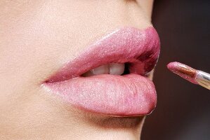 Frauenlippen werden mit rosa Lippenstift geschminkt, Close Up