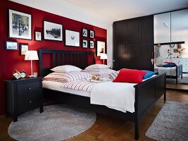 A bedroom with dark wooden furniture and pictures hung on dark red wall