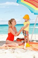 Mutter cremt kleine Tochter ein am Strand