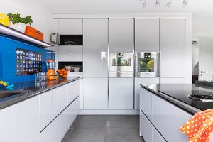 weiße Designerküche, seitlich über Küchenzeile blaue Glasplatte an Wand, mit integriertem Touchscreen