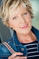 A portrait of an older woman in a denim jacket and a stripped shirt