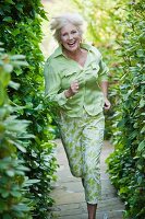 An older woman wearing a light green blouse and green-and-white trousers running in a garden
