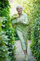 An older woman wearing a light green blouse and green-and-white trousers in a garden