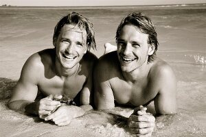 Zwillingsbrüder liegen am Strand im Wasser (Foto in Sepia)