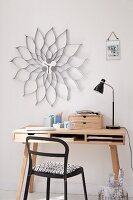 Nach klassischem Designer-Vorbild selbst gestaltete Wanduhr mit Blütenrahmen aus silberfarbener Wellpappe über kleinem Schreibtisch