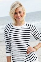 A blonde woman on a beach wearing a black and white striped, long-sleeved T-shirt