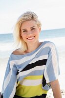A blonde woman on a beach wearing a striped, oversized shirt