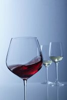 Rotwein schwappt im Glas, zwei Gläser Weißwein im Hintergrund