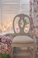 Antique, Swedish wooden chair flanked by vase of hydrangeas and floral curtain; tealights and roses on windowsill in background