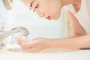 Asiatische Frau wäscht sich Gesicht am Waschbecken