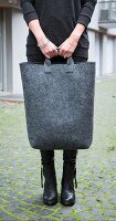 A woman holding a large bag made of grey felt