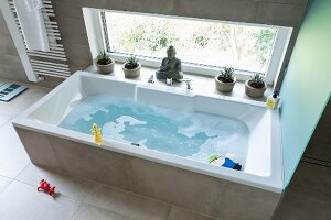 A bathtub filled with water and toys against a window in a modern bathroom