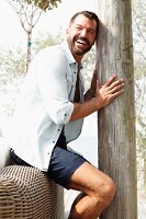 A man sitting the back of a piece of wicker furniture holding onto a wooden pole