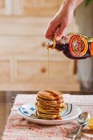 Maple syrup being poured onto a stack of pancakes