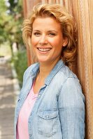 A blonde woman wearing a denim shirt leaning on a fence