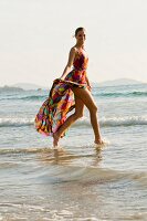 Blonde Frau in buntem Sommerkleid am Strand im flachen Meer