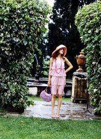 A young woman wearing a pink, flounced dress and a hat in a park
