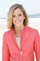 Young woman wearing pale shirt and salmon-pink leather jacket on beach