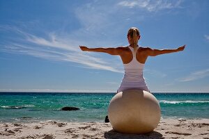 Frau macht Yogaübung auf Gymnastikball sitzend am Strand