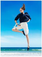 A woman wearing a dark blue jumper and white Bermuda shorts by the sea