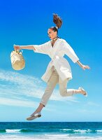 A woman wearing a white coat and beige trousers by the sea